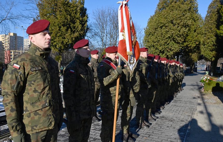 Szpaler żołnierzy w mundurach moro i bordowych beretach. Jeden z nich trzyma w ręku sztandar. 