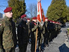 Szpaler żołnierzy w mundurach moro i bordowych beretach. Jeden z nich trzyma w ręku sztandar. 