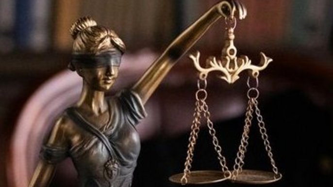 - grafika ilustracyjna. Figurka kobiety z przepaską na oczach i wagą szalkową w lewej ręce symbolizująca sprawiedliwość.