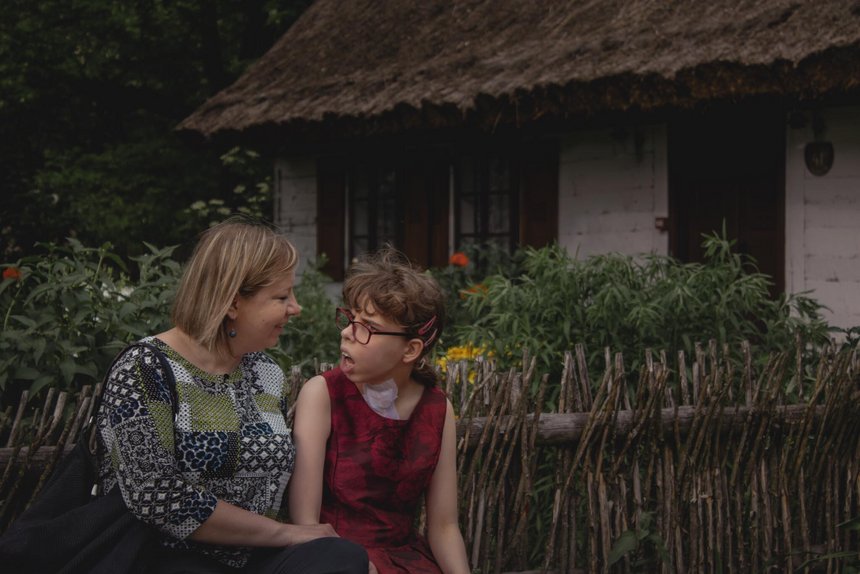 Julia i pani Monika siedzą na ławce. W tle drewniany dom z ogrodem.