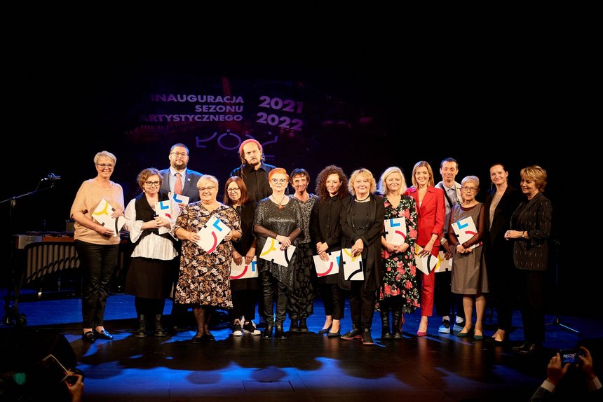 Na scenie teatralnej stoi grupa ludzi. W dłoniach trzymają listy gratulacyjne. Są to laureaci nagród. 