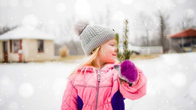  - Uśmiechnięta dziewczynka trzyma gałązkę świerku. W tle zimowy krajobraz.