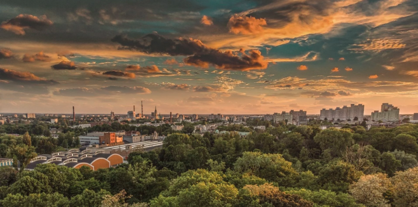 Panorama Łodzi na tle zachodzącego słońca. Ponad parkiem wysokie zabudowania na linii horyzontu.