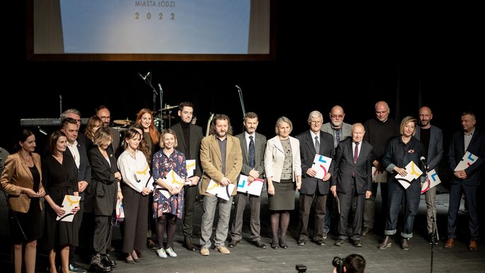  - Na scenie teatralnej stoi grupa ludzi. W dłoniach trzymają listy gratulacyjne. Są to laureaci nagród.